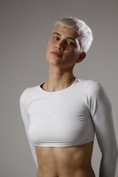Stylish portrait of a person with short hair and white crop top against a neutral background.