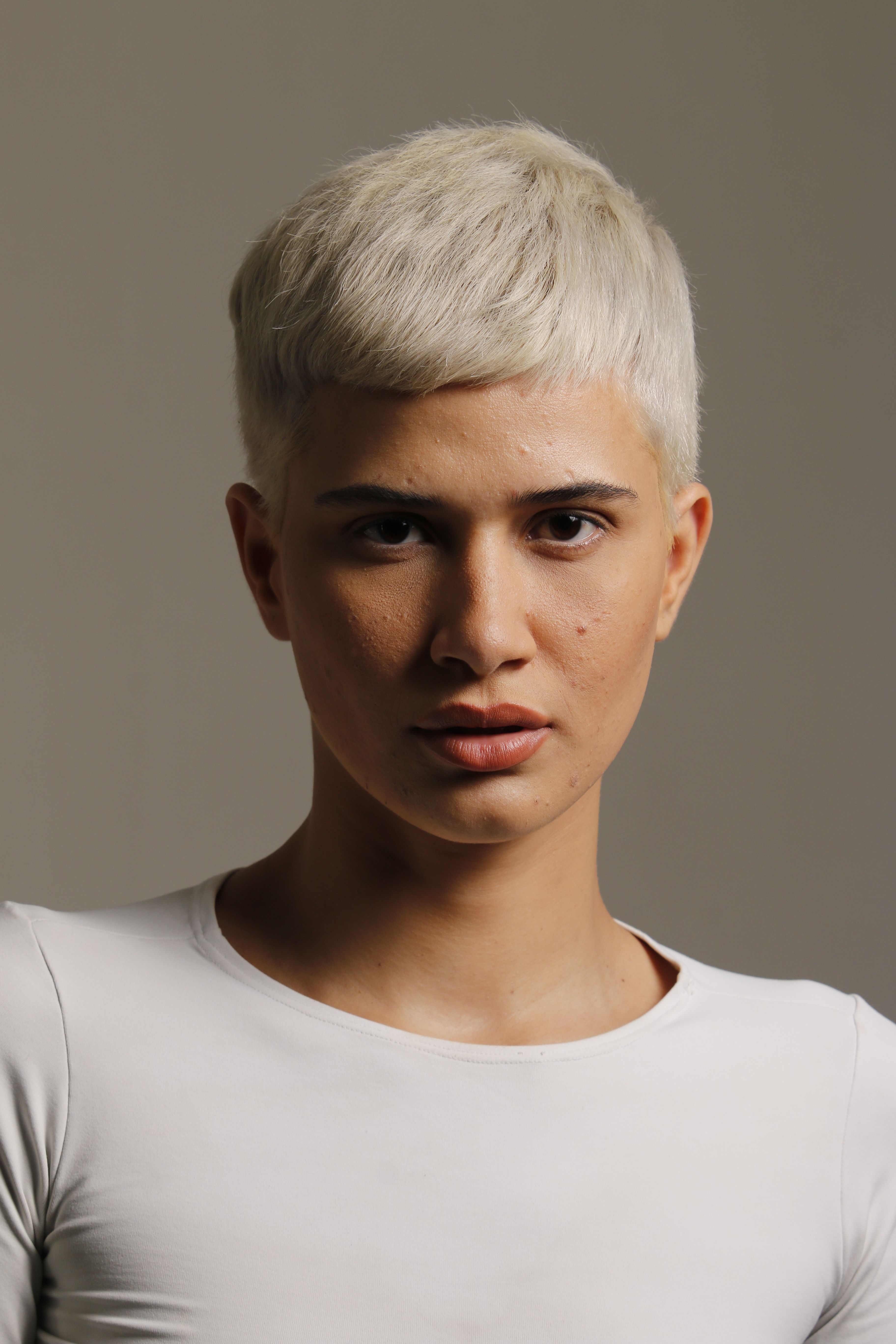Studio portrait of a person with short blonde hair in a white shirt.
