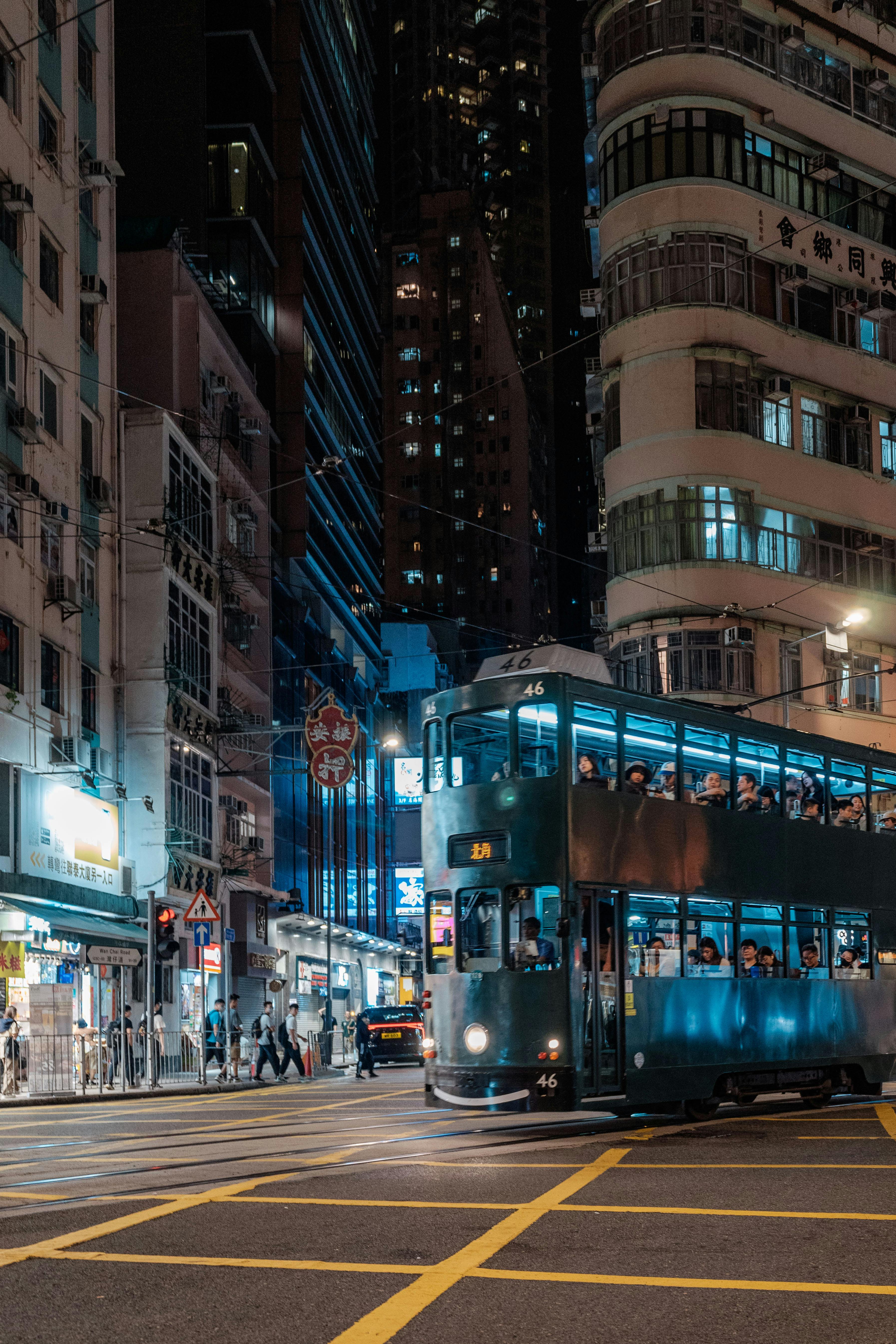 A double-decker tram travels through Hong Kong Island's bustling streets at night, showcasing urban life.
