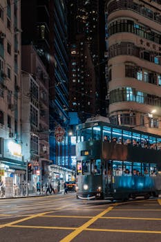 A double-decker tram travels through Hong Kong Island's bustling streets at night, showcasing urban life.