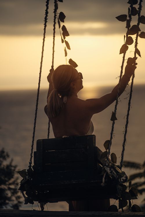 Free A woman enjoys a peaceful swing ride at sunset by the ocean, embraced by nature. Stock Photo