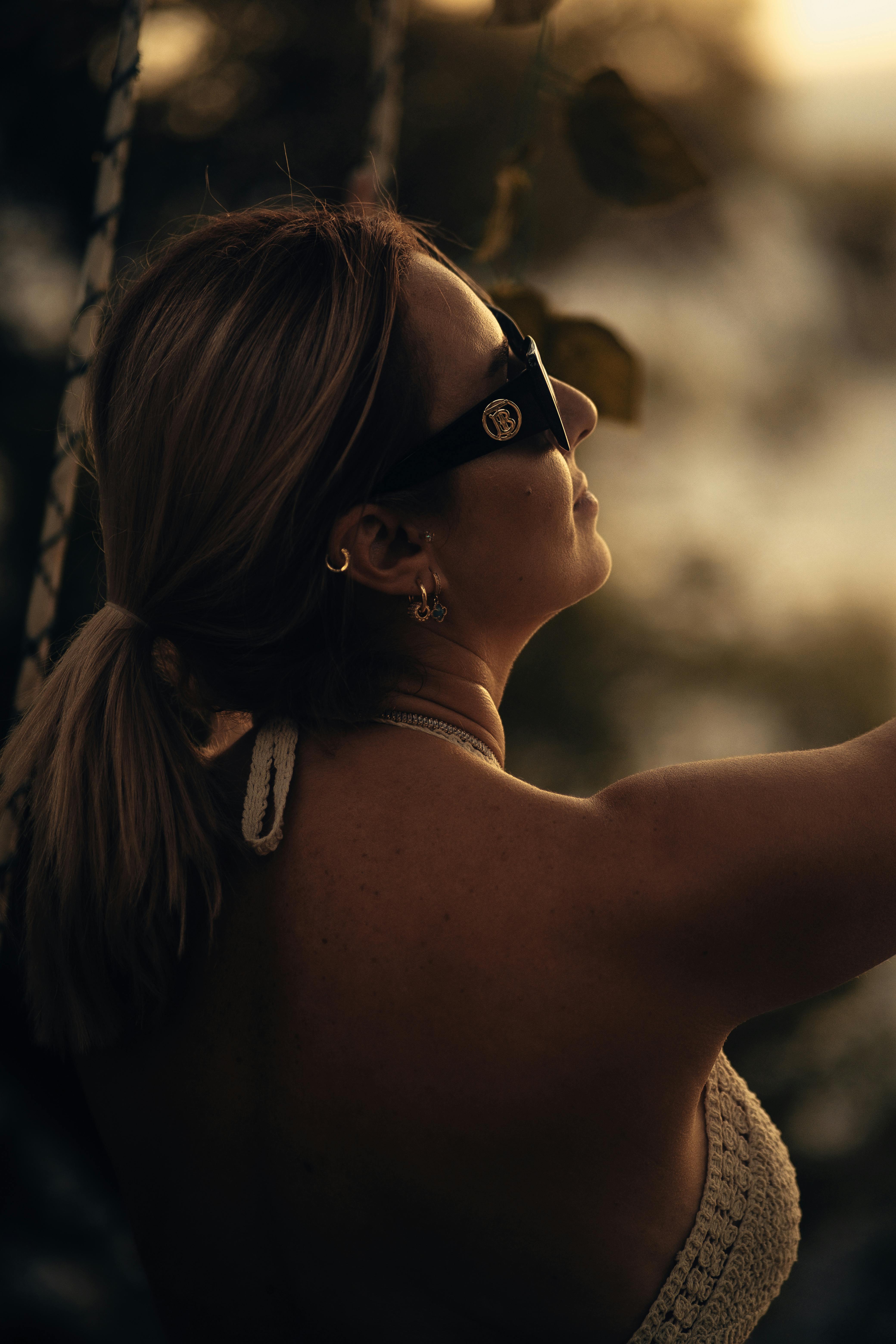 A stylish woman wearing sunglasses enjoys the sunset outdoors, capturing a chic summer moment.