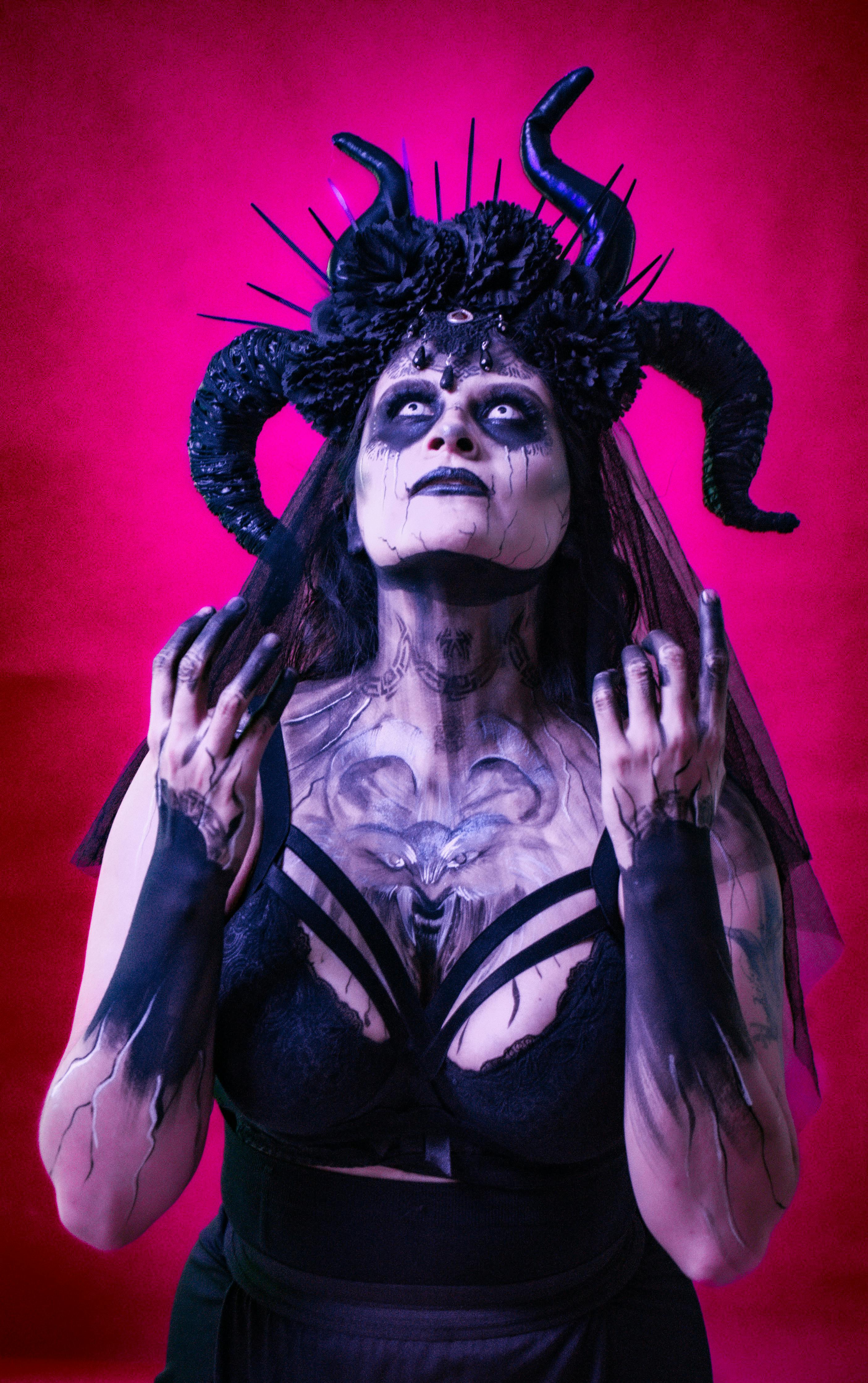 Gratuit Portrait de femme à thème gothique avec une coiffe à cornes et une peinture faciale complexe sur fond rose vif. Photos