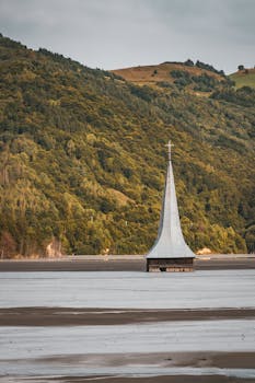 夏日，一座孤独的教堂塔楼矗立在宁静的湖泊中，四周群山环绕