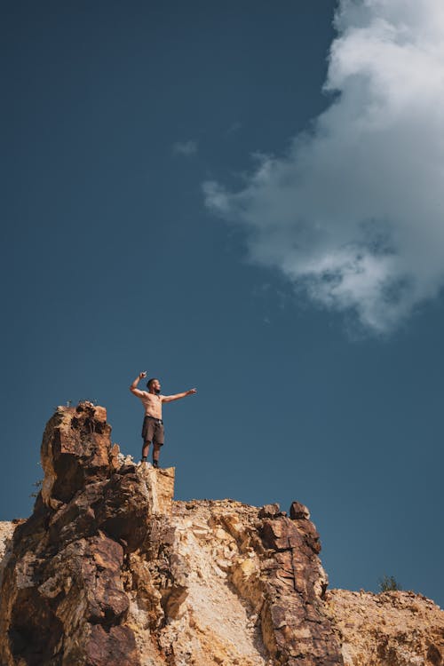 Topless Man Standing on Cliff