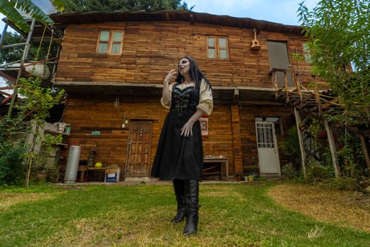 Adult female in vampire costume in front of rustic wooden cabin.