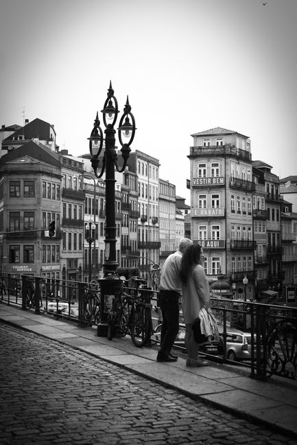 Black and white photo of a couple embracing on a street with historic buildings.