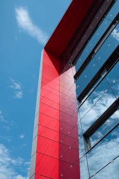 Vibrant modern building with red facade and glass windows under a clear blue sky.