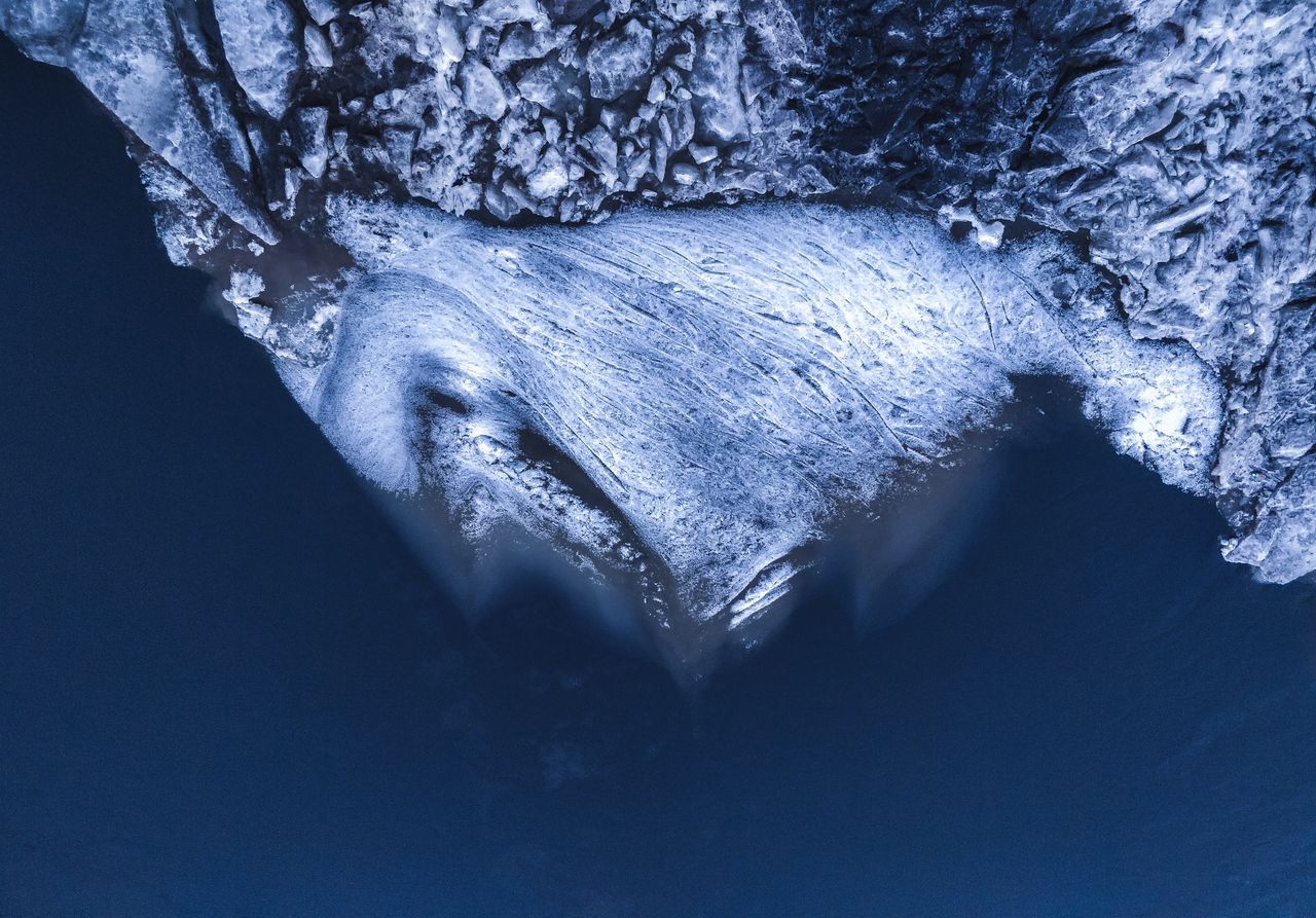 drone shot capturing a frozen iceberg surrounded by dark blue waters s