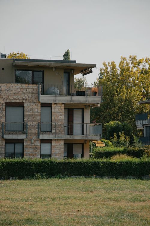 Free Modern Hungarian apartment building with stone facade and lush greenery on a summer day. Stock Photo