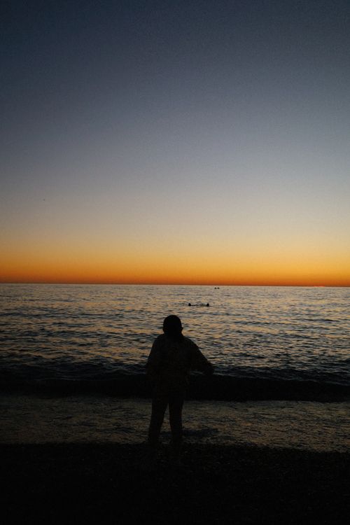 Free A silhouette of a person standing by the ocean during a peaceful sunset. Stock Photo