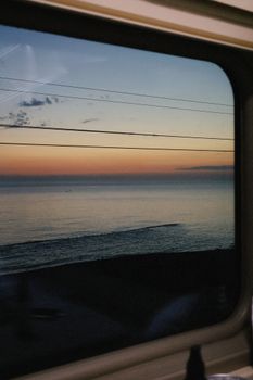 Tranquil sunset view over ocean from train window, serene landscape.