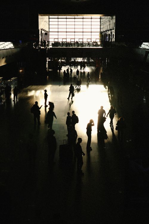 Free Silhouetted travelers in a dimly lit airport terminal with a bright window. Stock Photo