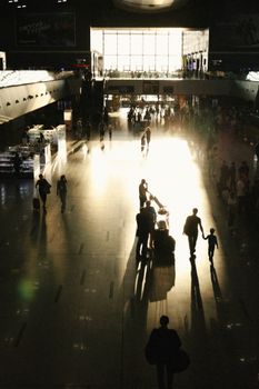 Silhouettes of travelers walking through a sunlit airport terminal in warm light.