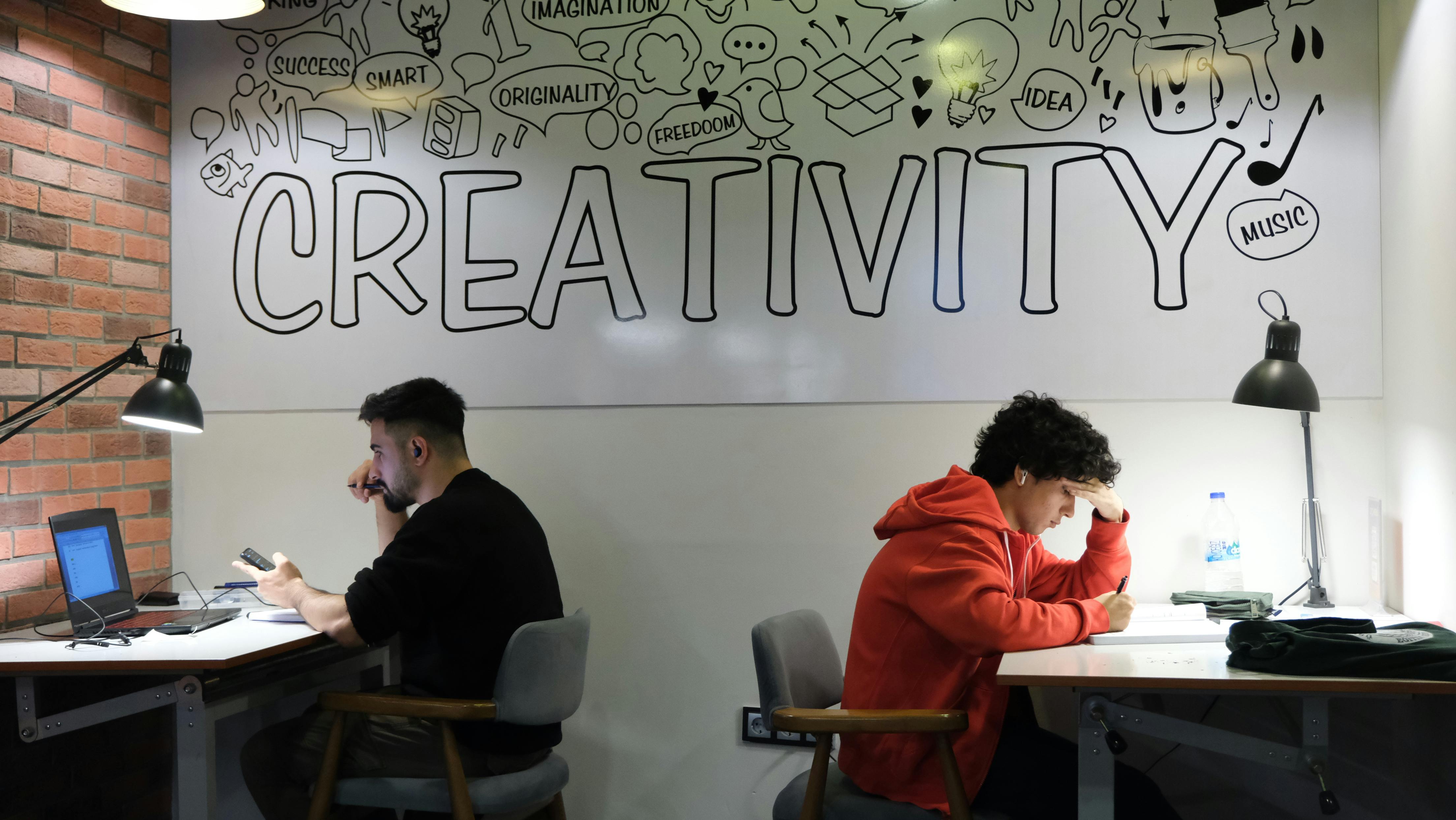 Two individuals working in a creative workspace with artistic wall decor.