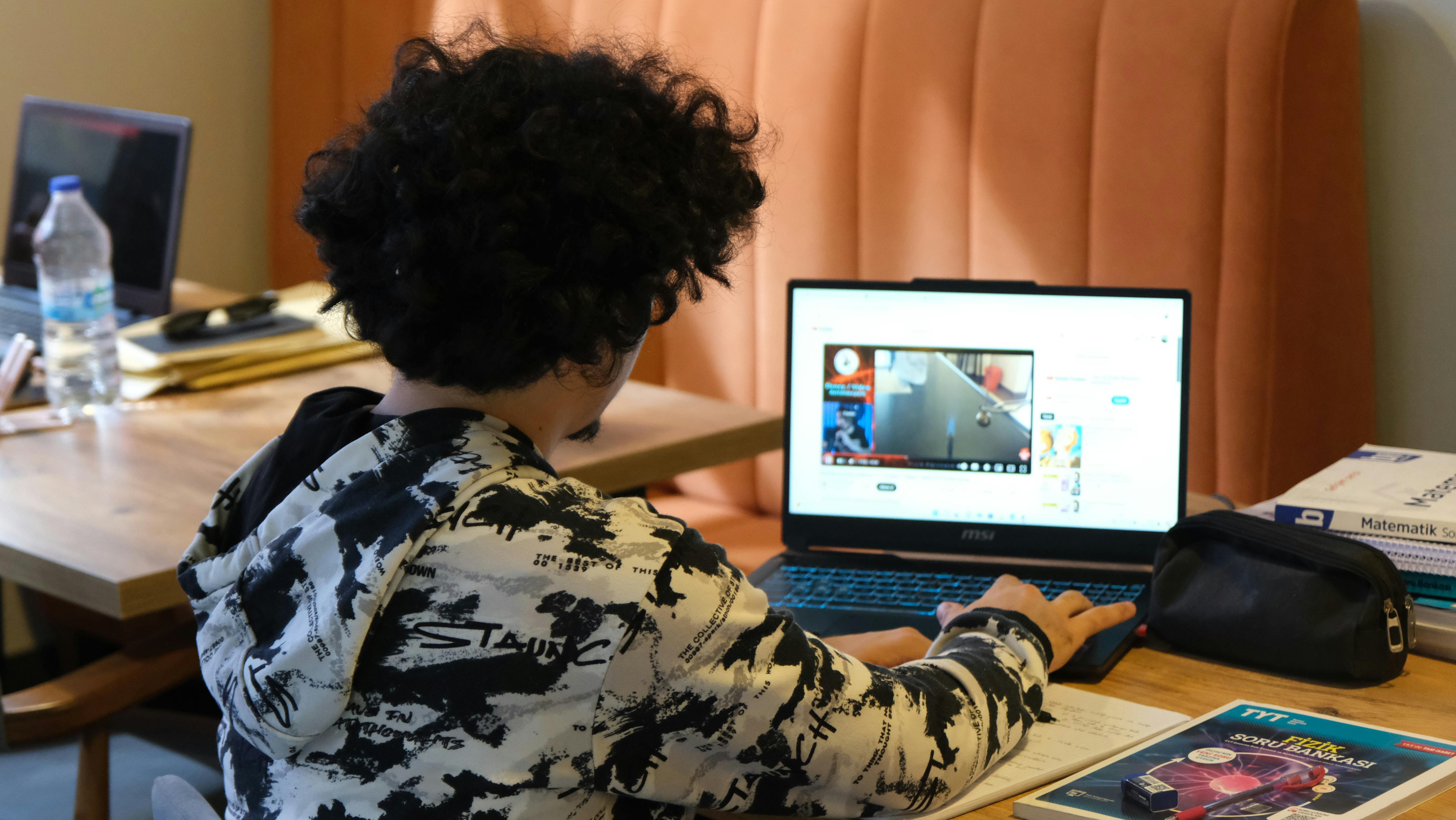 Teenager using a laptop for learning at home, surrounded by study materials and books.