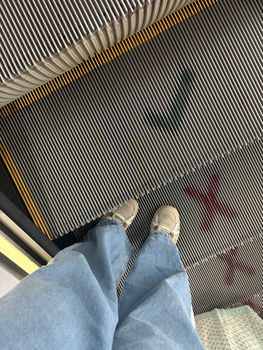 Perspective shot of feet in denim jeans on an escalator step, indoors.