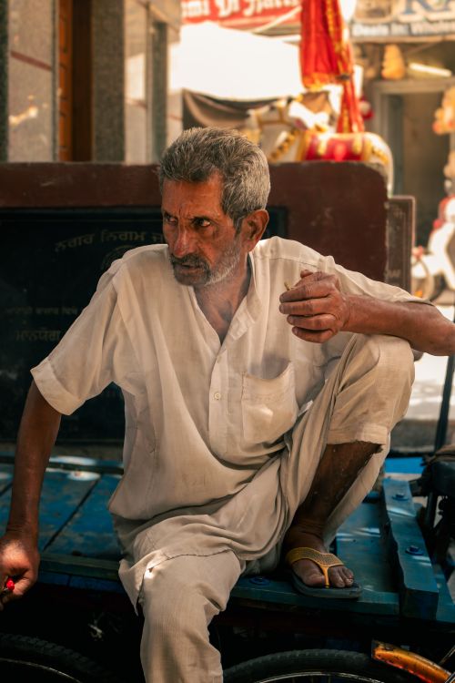 Free Elderly rickshaw puller sits in Jalandhar street, showcasing daily life and resilience in summer. Stock Photo
