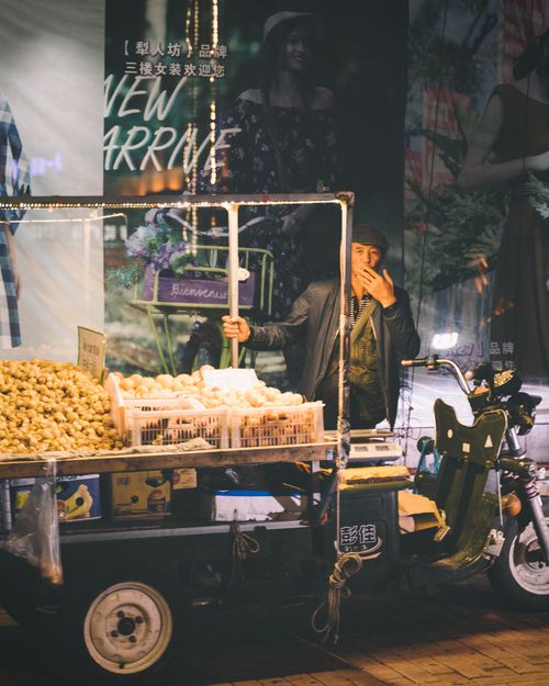 Free Street vendor at night market selling food on a motorized cart with bustling urban backdrop. Stock Photo