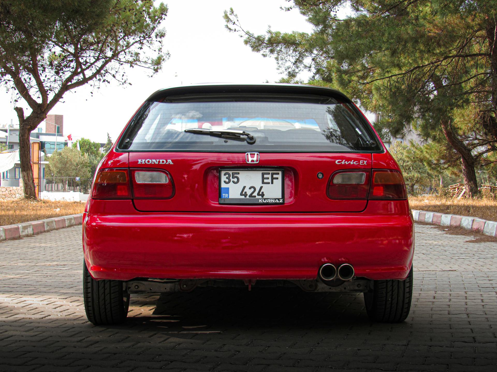 Rear view of a red Honda Civic EX car parked on a tree-lined driveway.