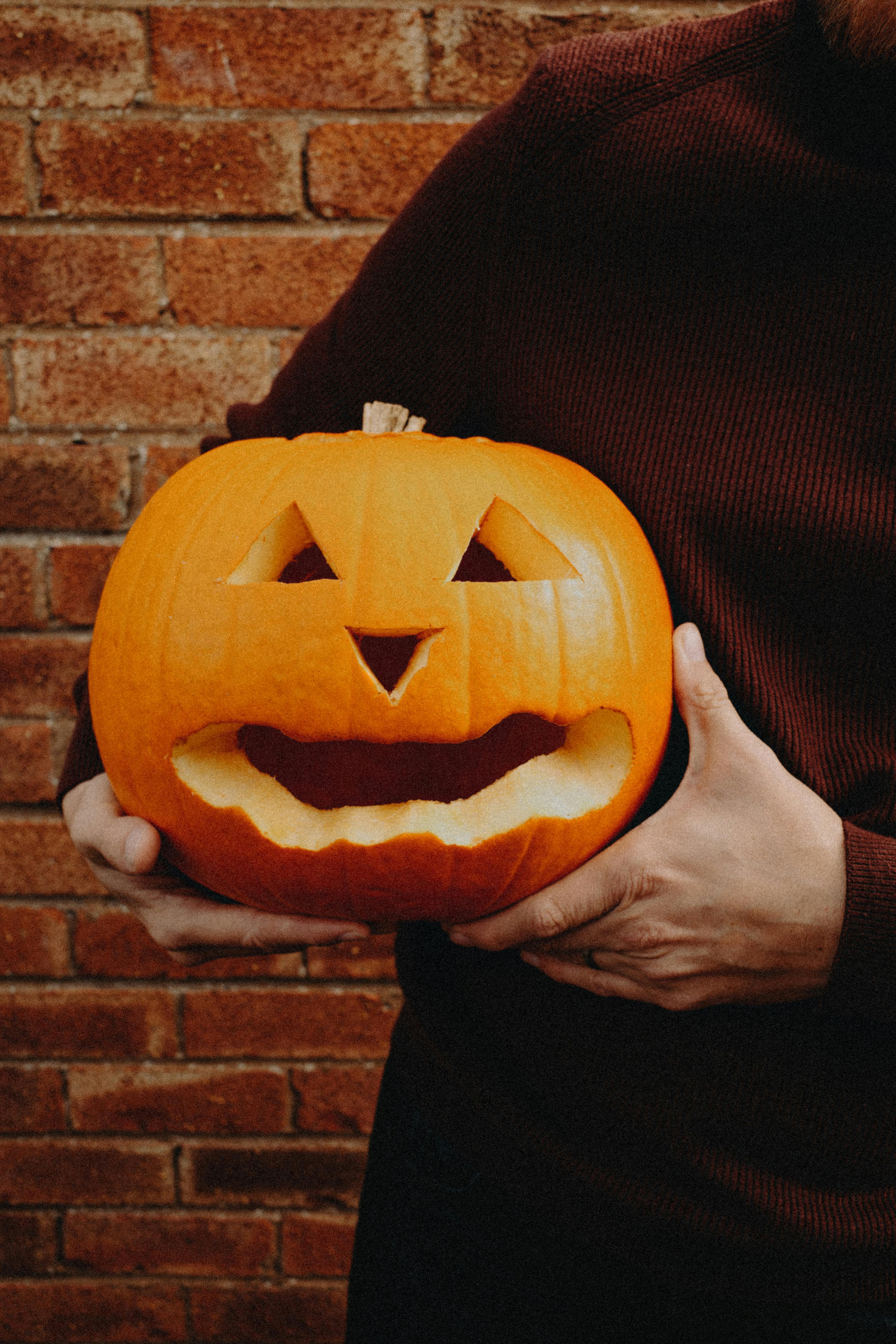 A carved jack-o'-lantern held by an adult against a brick wall, perfect for Halloween.