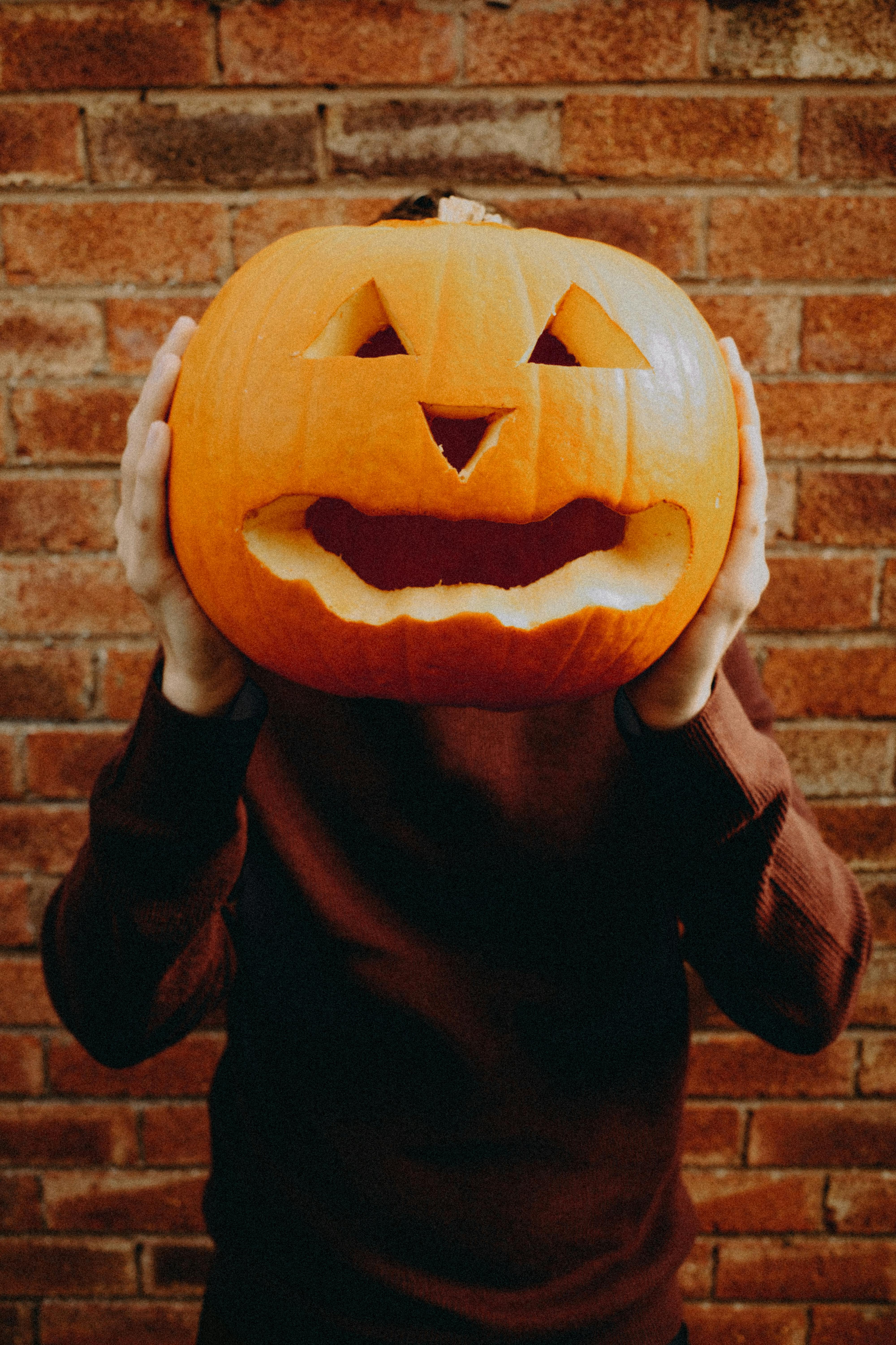 Person holding carved pumpkin in front of their face against a brick wall.