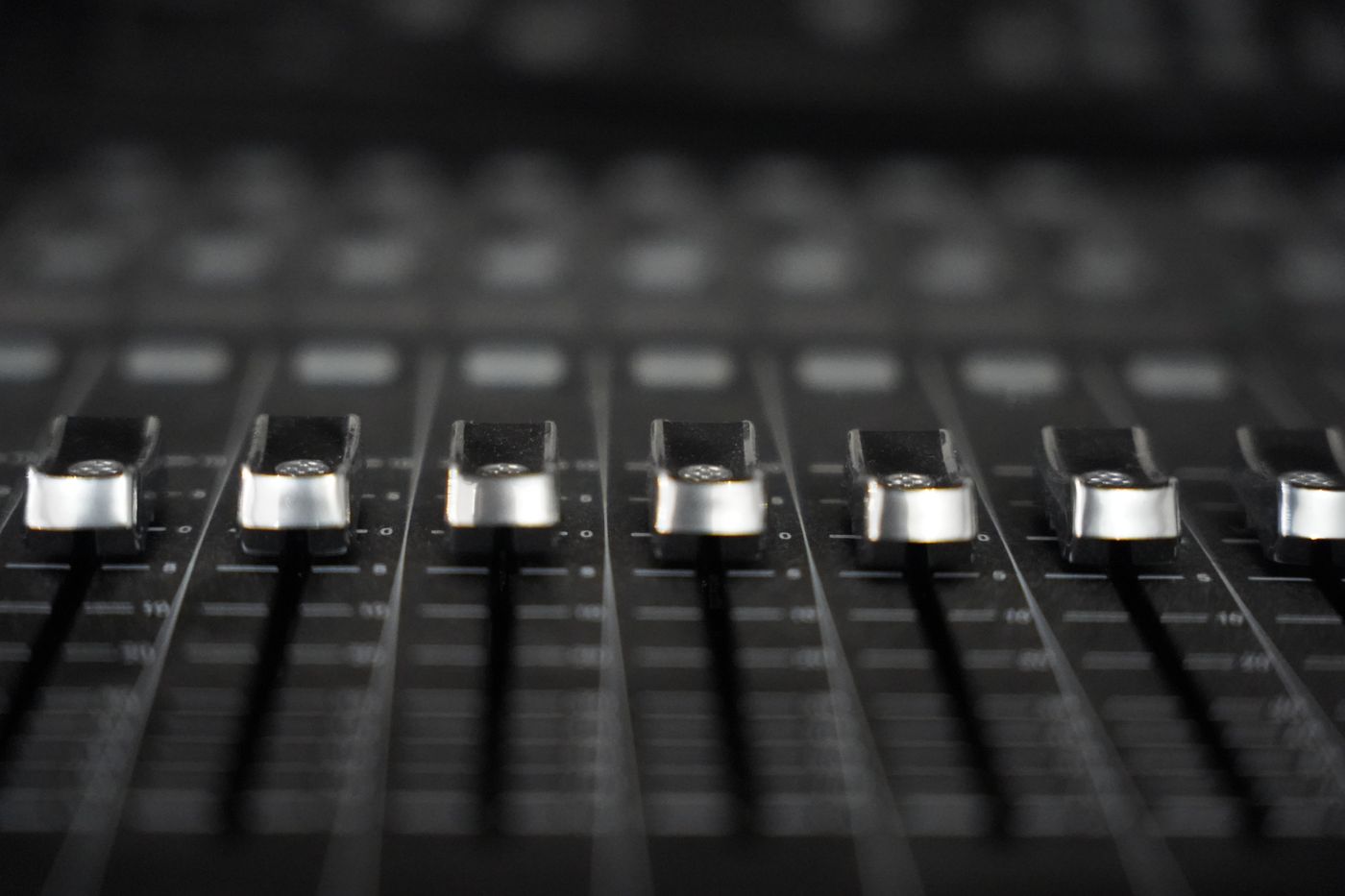 A row of silver faders on a black mixing console