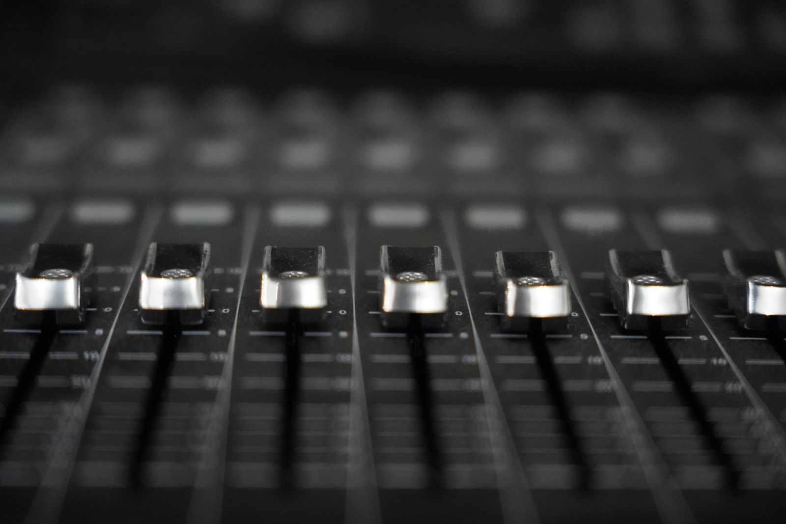 A row of silver faders on a black mixing console in soft focus