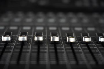 A row of silver faders on a black mixing console