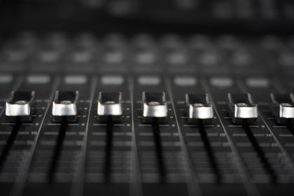 A row of silver faders on a black mixing console