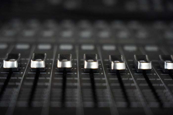 A row of silver faders on a black mixing console