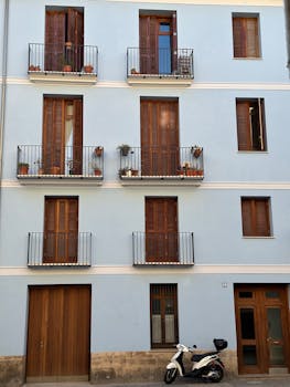 Elegant urban apartment facade with balconies, plants, and a parked scooter.