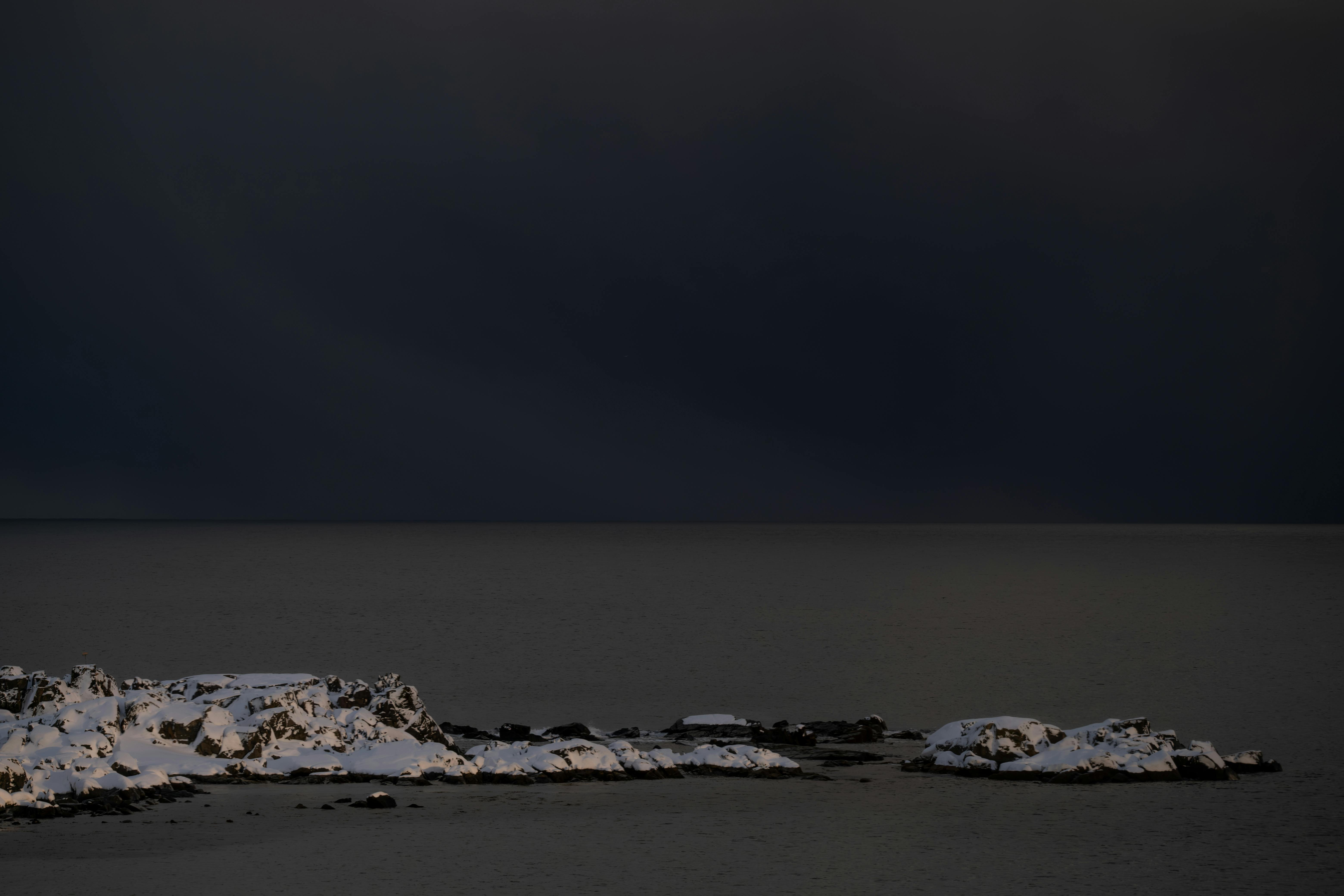 Free Snow-covered rocky coast under dark stormy sky, creating a dramatic winter scene. Stock Photo