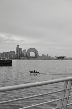 A boat sails in a harbor with a striking city skyline featuring an arch building.
