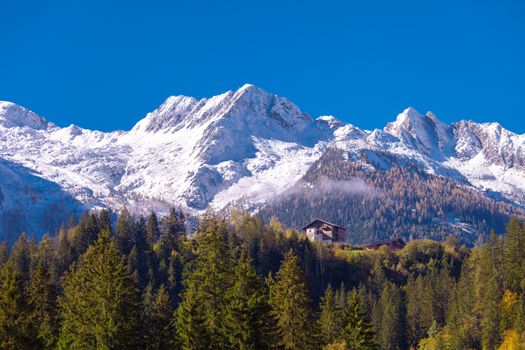 Alpine house nestled against majestic snowy mountains under a clear blue sky.