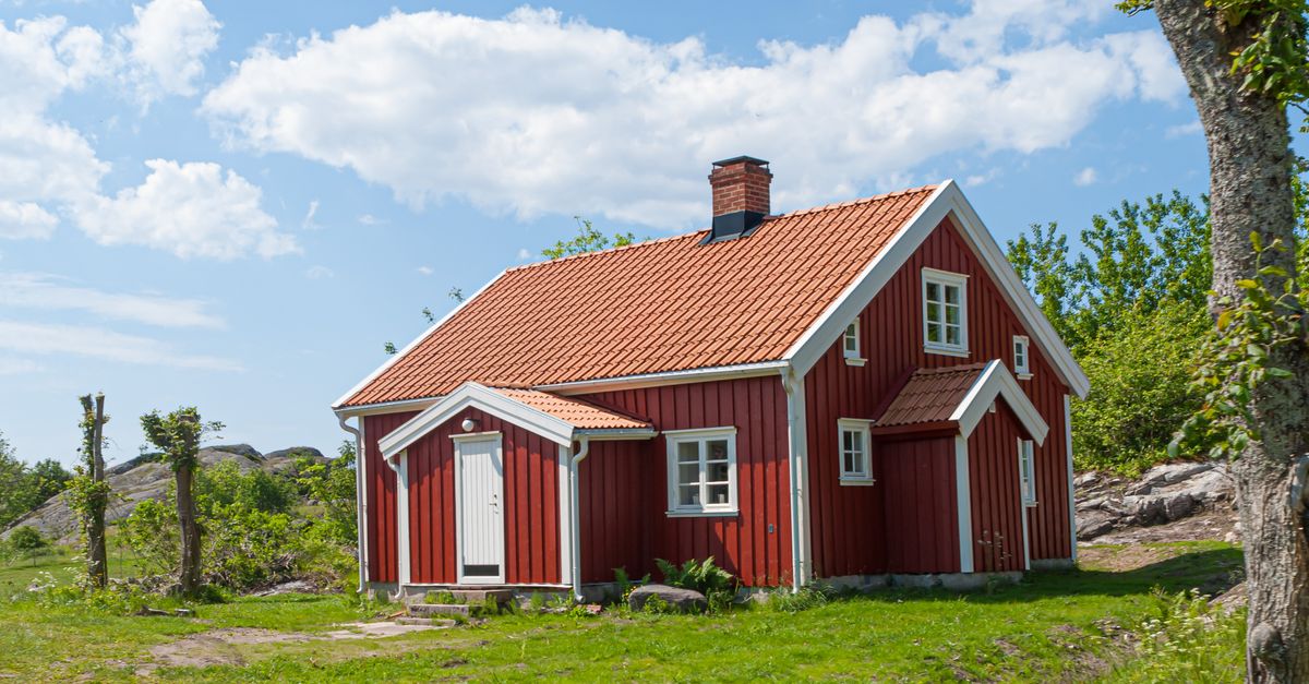 Picturesque red cottage under blue skies, surrounded by lush greenery in a rural setting.