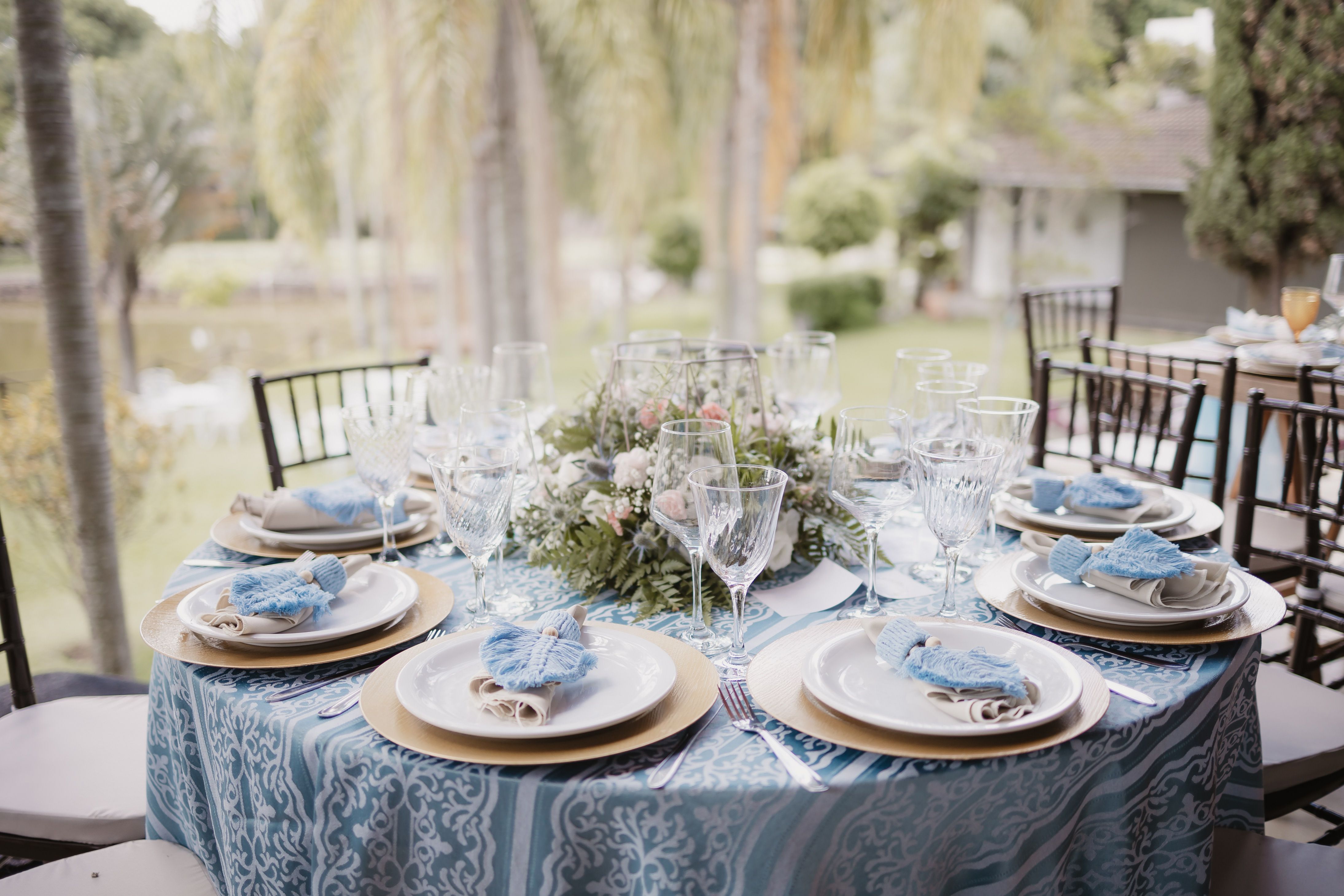 Chic outdoor dining table with floral centerpiece and elegant dishware set against a lush backdrop.