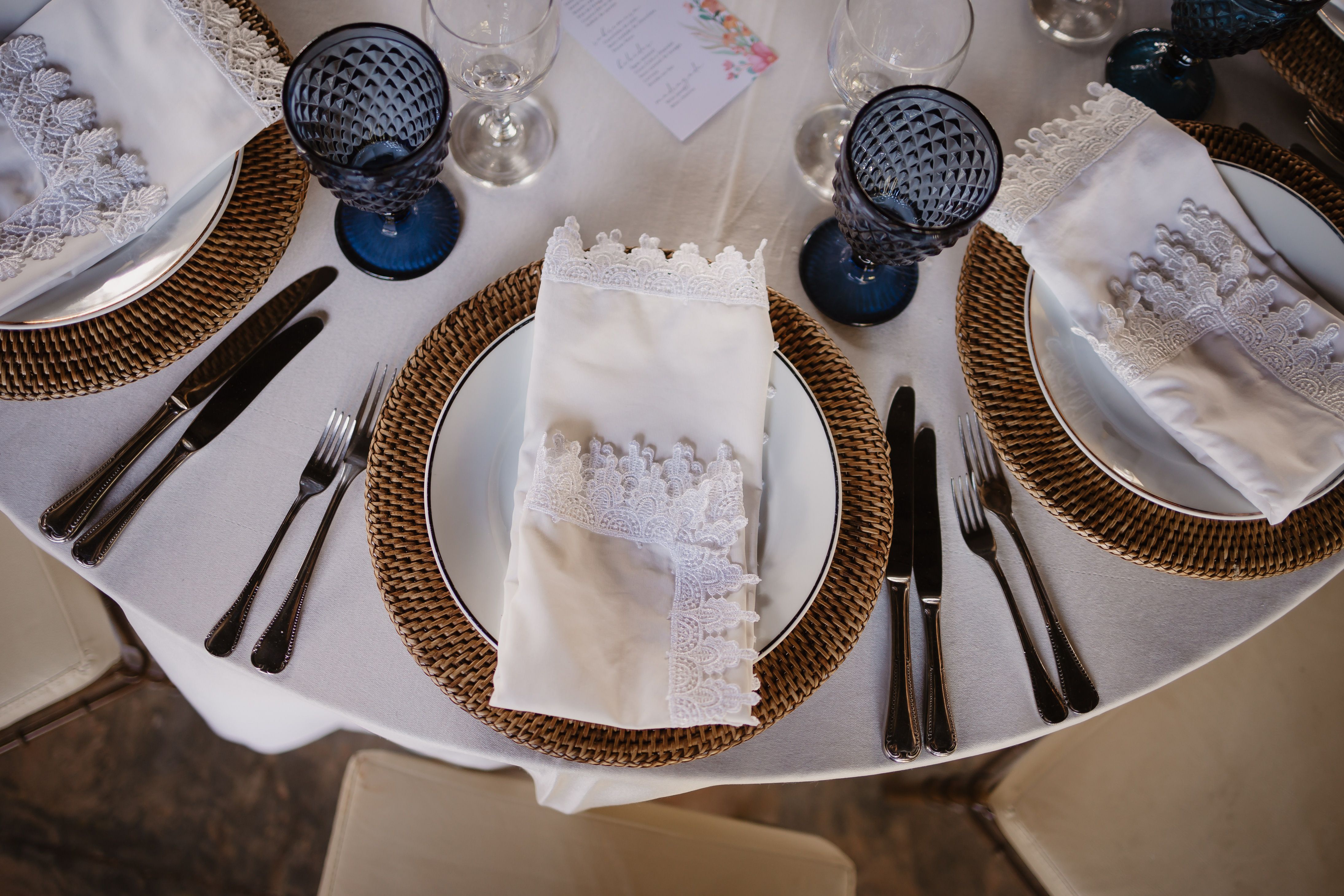 A beautifully arranged dining setup with lace napkins, wicker placemats, and blue glassware.