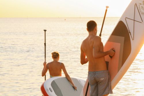 Free A couple enjoys paddleboarding at sunset on a serene Barcelona beach, capturing leisure and adventure. Stock Photo