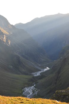 Discover the serene beauty of a mountain valley in Himachal Pradesh with sunlit peaks and a winding river.