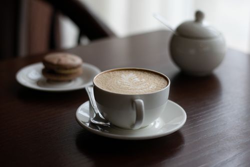 Free Serene composition featuring a cappuccino and macarons on a wooden table, exuding a cozy ambiance. Stock Photo