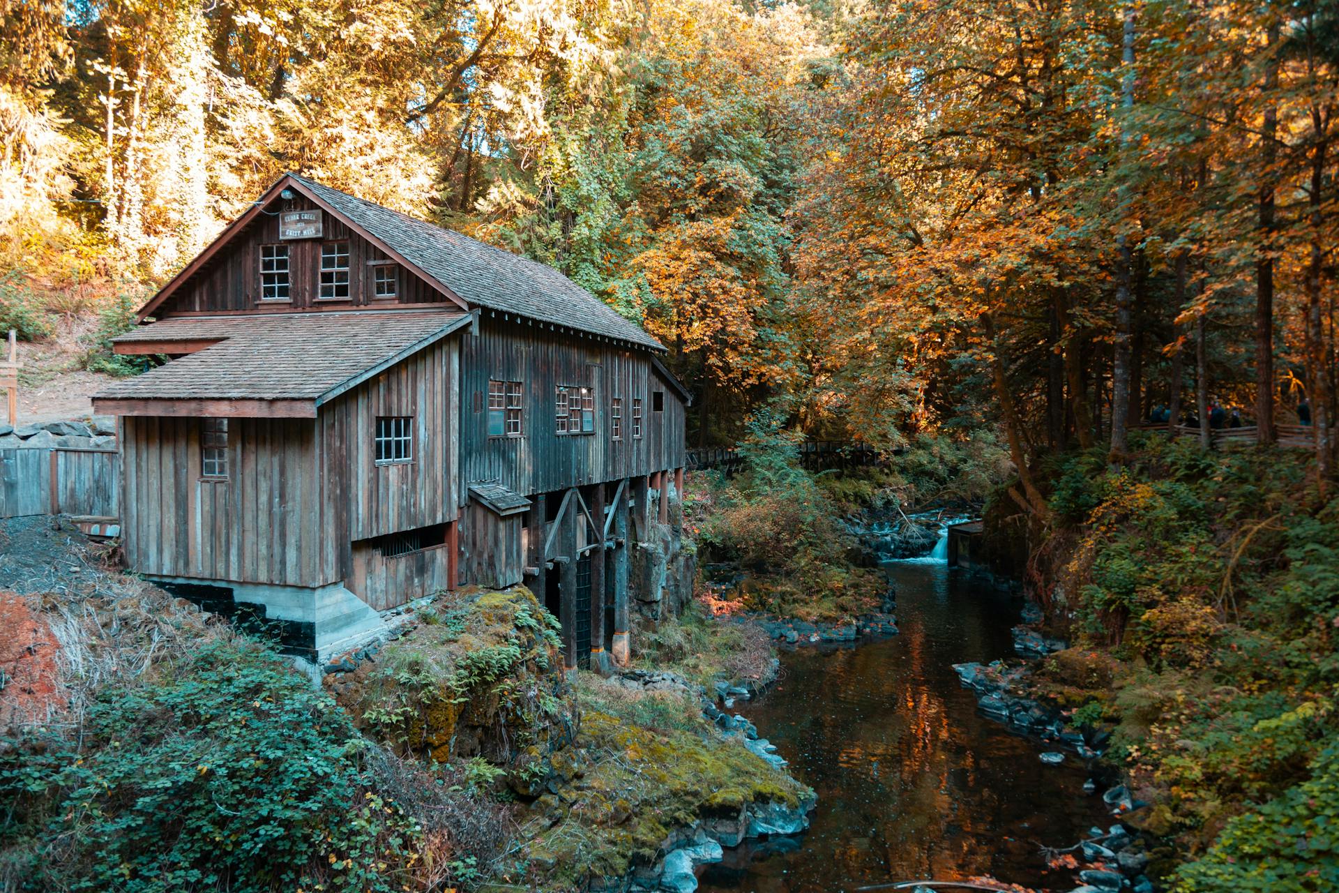 A charming grist mill beside a scenic creek, surrounded by vibrant autumn trees in a peaceful forest.