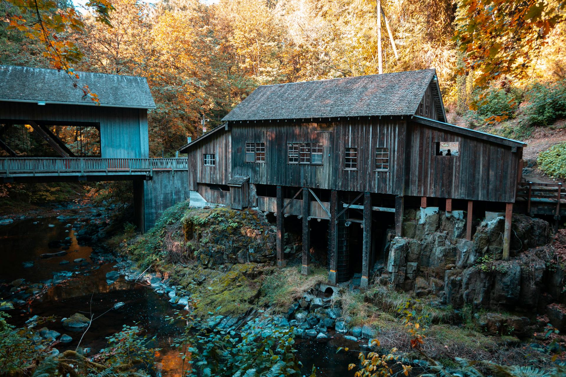 A scenic view of a historic grist mill surrounded by vibrant autumn foliage and a creek.