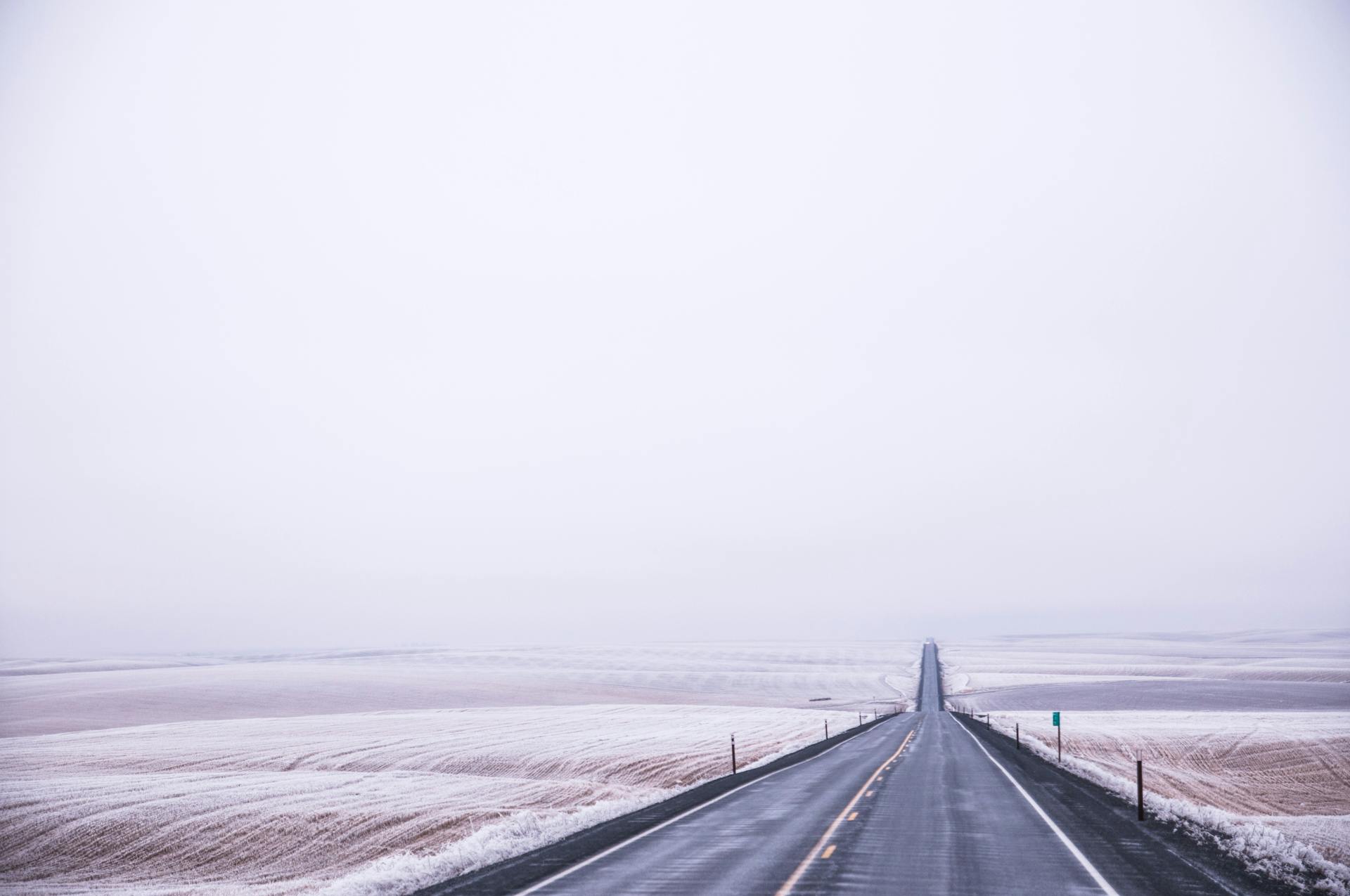 Long empty road stretching through snow-covered fields, capturing solitude and serenity.