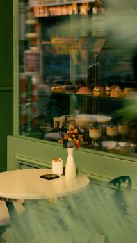 Elegant cafe table with a candle and vase near a pastry-filled window display.