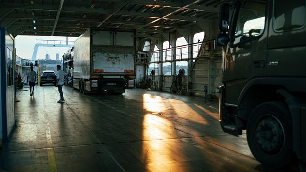 A serene view inside a ferry cargo area with trucks at sunset.