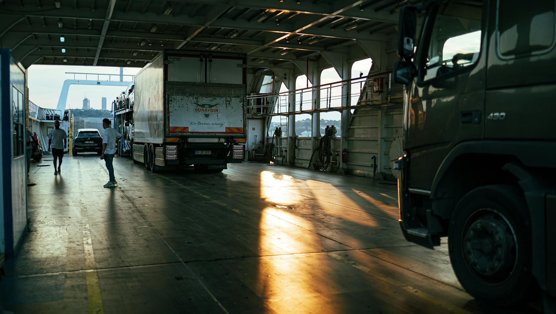 A serene view inside a ferry cargo area with trucks at sunset.