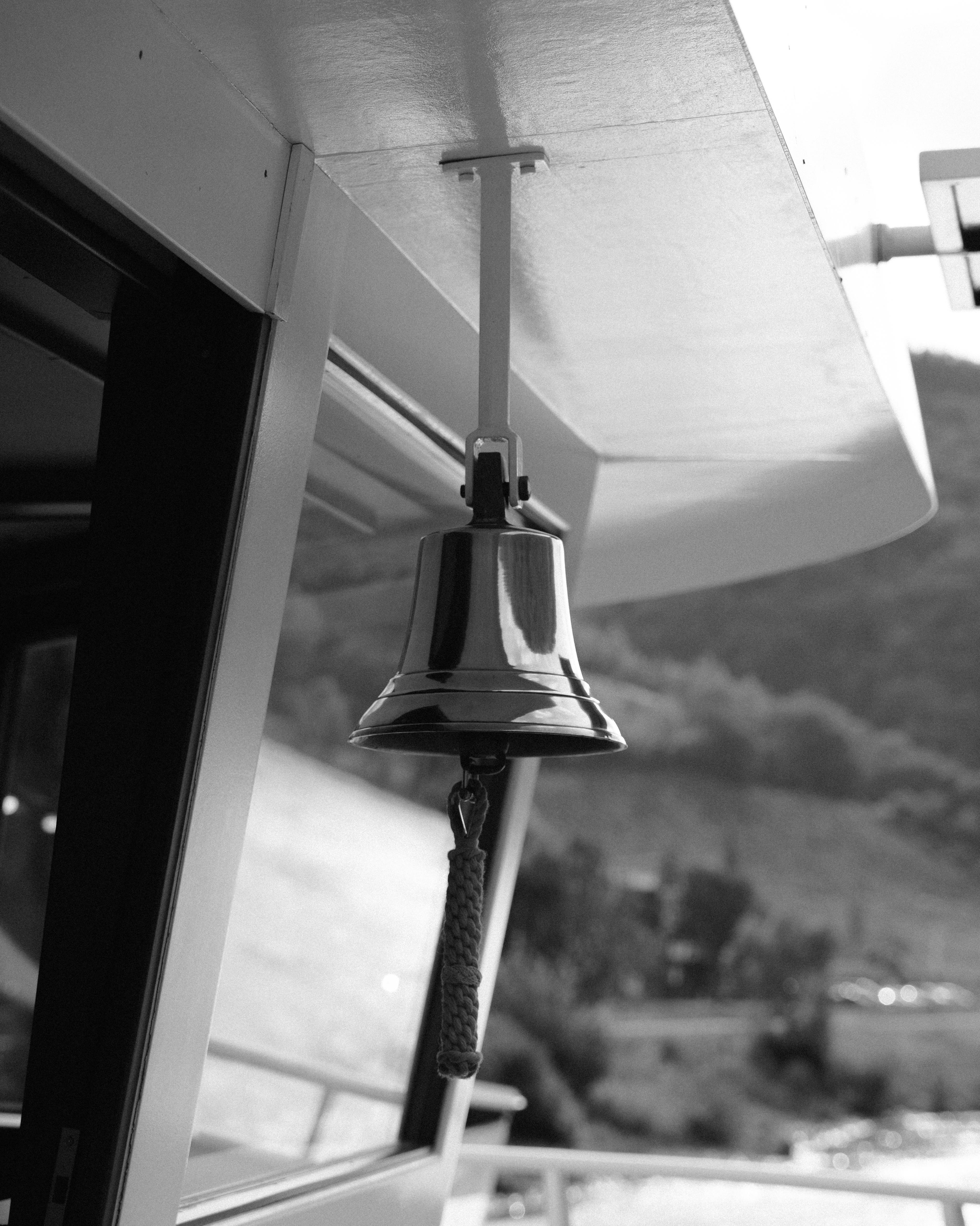 Monochrome close-up of a ship's bell against a scenic backdrop.
