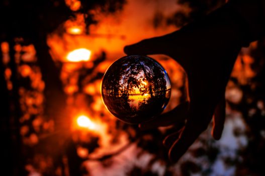 Vibrant sunset scene reflected in a glass sphere held by a silhouetted hand.