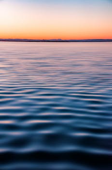 Peaceful ocean view at twilight with calm water and soft ripples under a colorful sky.